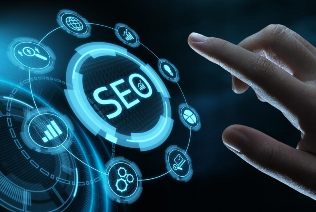 Uma mão toca uma interface digital holográfica azul com o texto "SEO" no centro, rodeado por diversos ícones de marketing digital e análise de dados.